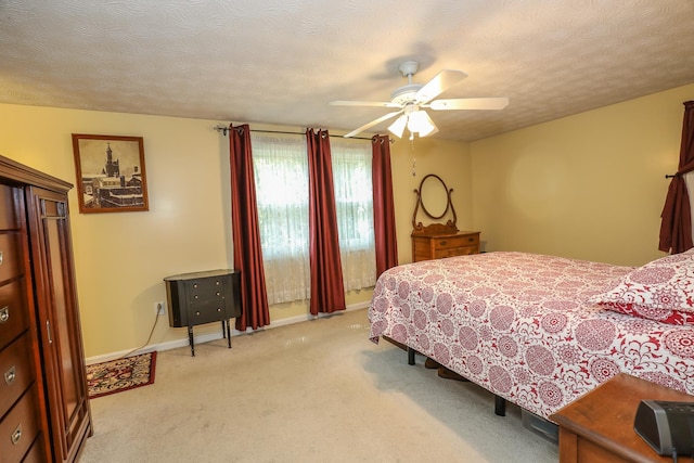 bedroom featuring light colored carpet, a ceiling fan, baseboards, and a textured ceiling