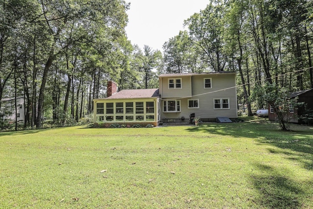 rear view of house with a sunroom, a yard, and a chimney