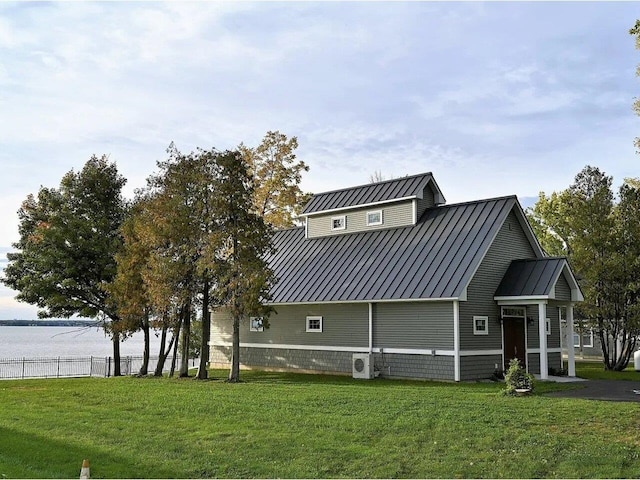 exterior space with a water view, a front lawn, fence, and metal roof