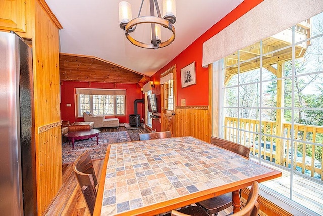 dining space featuring a wood stove, wainscoting, wood finished floors, wooden walls, and a notable chandelier