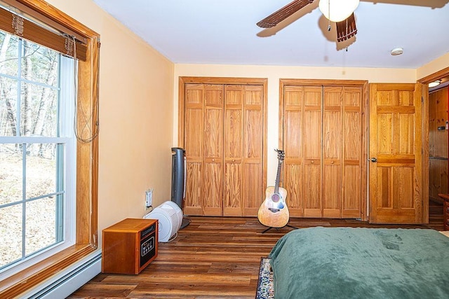bedroom featuring dark wood finished floors, ceiling fan, a baseboard heating unit, and two closets