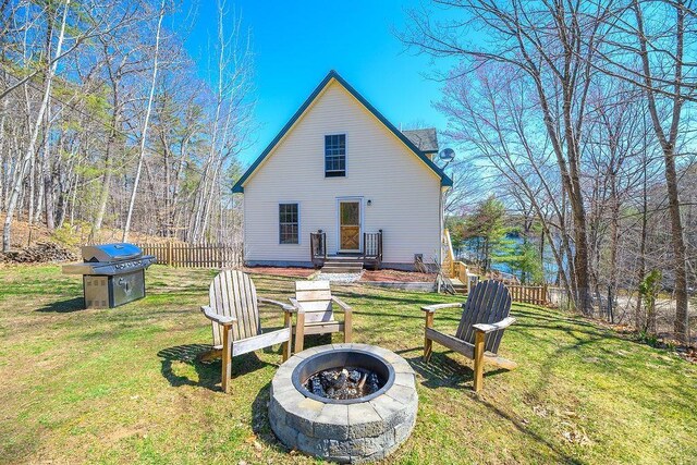 back of house featuring a lawn, a fire pit, and fence