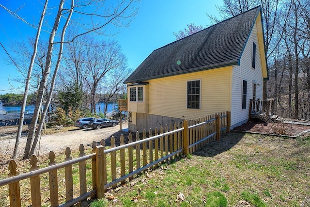 view of property exterior featuring a water view, a shingled roof, and fence private yard