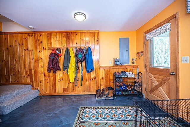 mudroom featuring wooden walls, finished concrete flooring, electric panel, and a wainscoted wall
