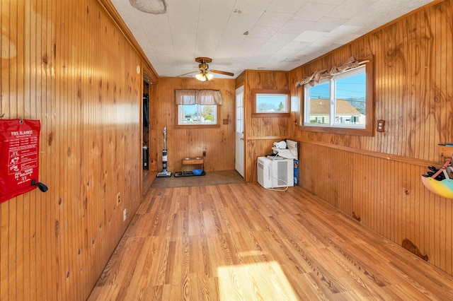 unfurnished room with light wood-type flooring, wood walls, and ceiling fan
