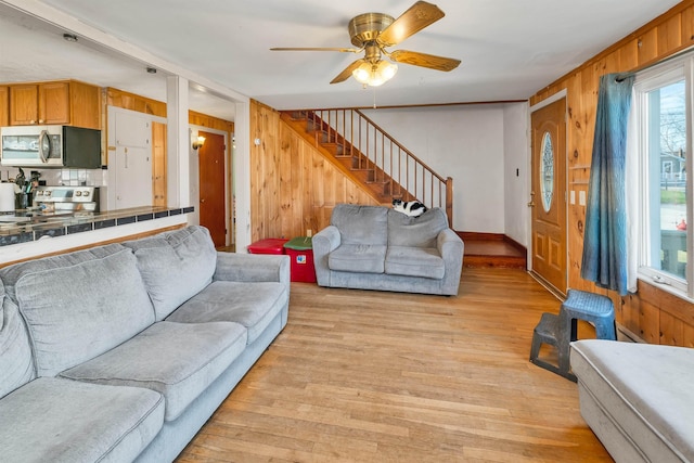 living area with a ceiling fan, wood walls, stairway, and light wood-style floors