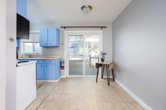 kitchen featuring light countertops, blue cabinetry, a sink, and baseboards