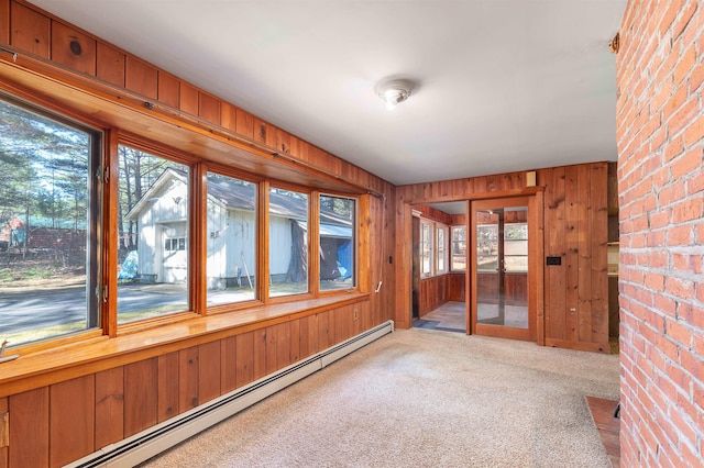 unfurnished sunroom with plenty of natural light, carpet floors, a baseboard radiator, and wood walls
