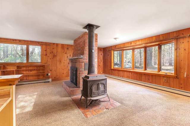 unfurnished living room with carpet floors, wooden walls, baseboard heating, and a wood stove