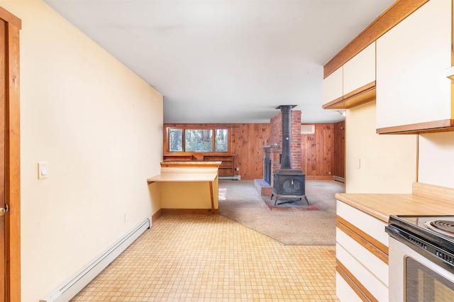 kitchen featuring a wood stove, light floors, wooden walls, baseboard heating, and white cabinetry