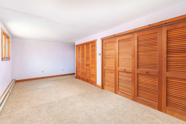unfurnished bedroom featuring carpet flooring, baseboards, multiple closets, and a baseboard radiator