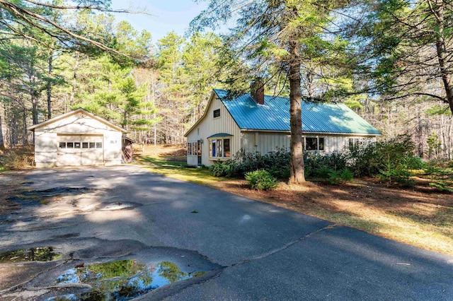 view of side of home featuring aphalt driveway, a garage, an outbuilding, a chimney, and metal roof