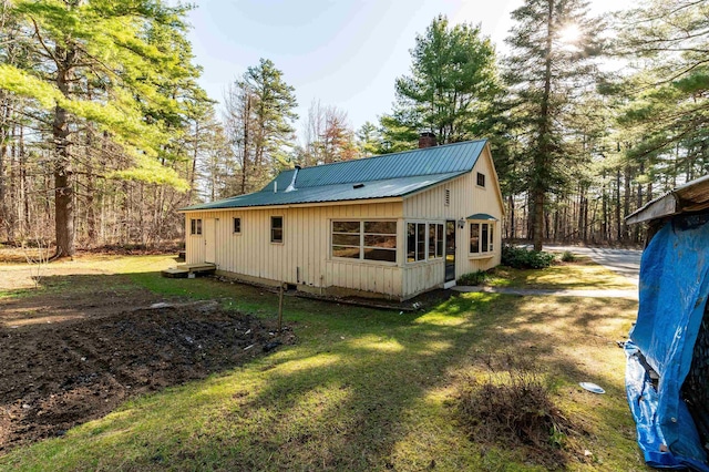 rear view of property with a yard, board and batten siding, a chimney, and metal roof