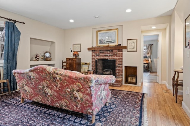 living area featuring a brick fireplace, recessed lighting, baseboards, and light wood finished floors