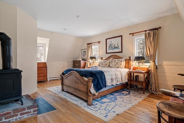 bedroom featuring a wood stove, a baseboard heating unit, and hardwood / wood-style flooring