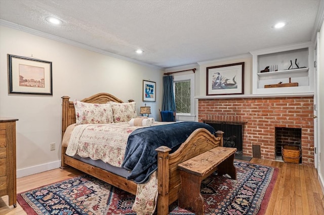 bedroom featuring crown molding, a fireplace, light wood-style floors, a textured ceiling, and baseboards