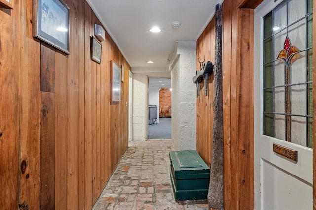 corridor featuring recessed lighting, wood walls, and brick floor