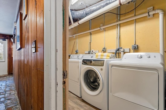 laundry area featuring wooden walls, separate washer and dryer, laundry area, and wood finished floors