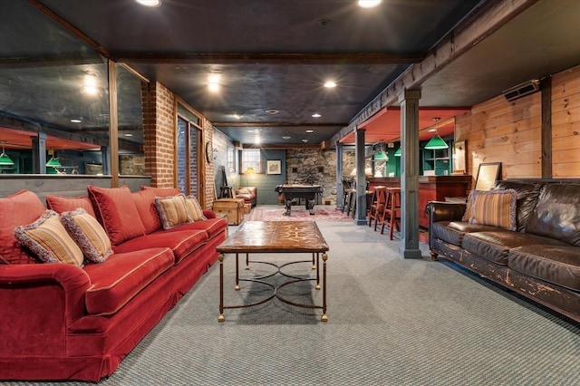 carpeted living area featuring wooden walls, indoor bar, and decorative columns