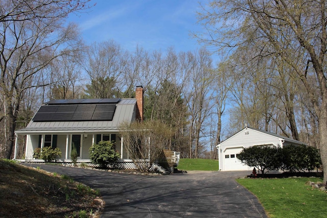 view of property exterior featuring roof mounted solar panels, an outbuilding, a chimney, covered porch, and metal roof