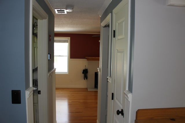 hallway featuring a textured ceiling, visible vents, wood finished floors, and a wainscoted wall