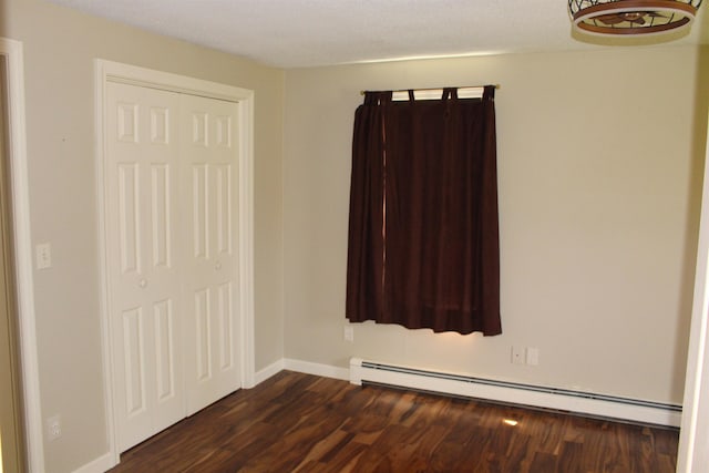 unfurnished bedroom with baseboards, a baseboard radiator, a closet, and dark wood-style floors