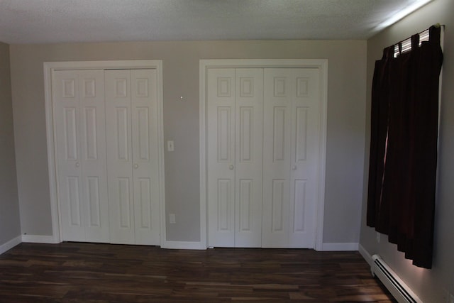 unfurnished bedroom with multiple closets, baseboards, a baseboard heating unit, and dark wood finished floors