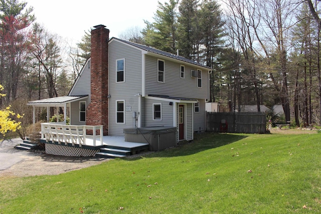 rear view of house featuring fence, a deck, a chimney, a lawn, and a hot tub