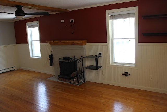 unfurnished living room featuring a ceiling fan, light wood-style floors, beam ceiling, and a wainscoted wall