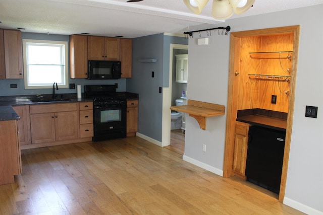 kitchen featuring light wood-style flooring, brown cabinets, a sink, and black appliances