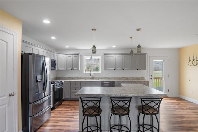 kitchen with appliances with stainless steel finishes, a sink, a kitchen breakfast bar, gray cabinets, and wood finished floors