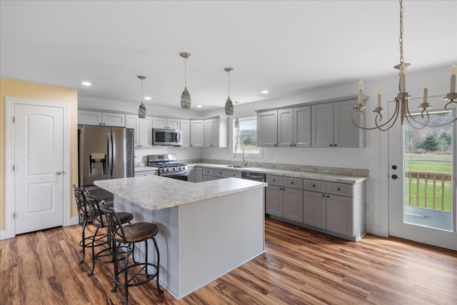 kitchen with a kitchen bar, gray cabinetry, light countertops, a sink, and stainless steel appliances
