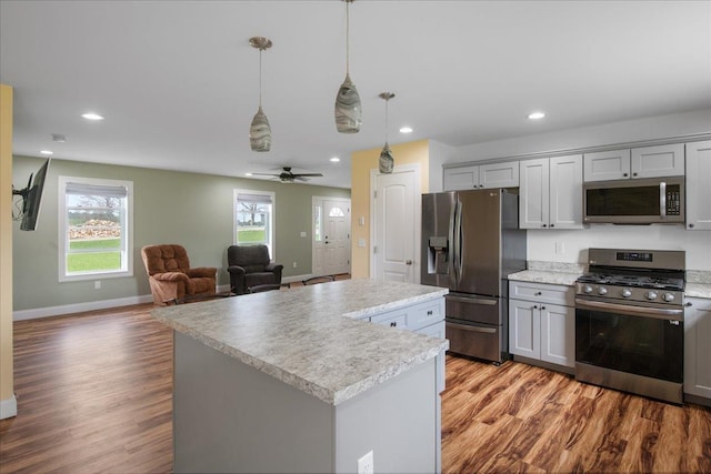 kitchen with wood finished floors, a kitchen island, light countertops, gray cabinets, and stainless steel appliances