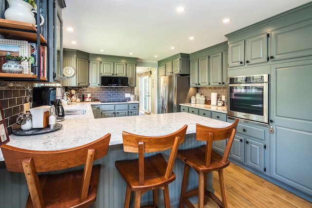 kitchen with green cabinetry, light wood-style floors, a peninsula, decorative backsplash, and black appliances