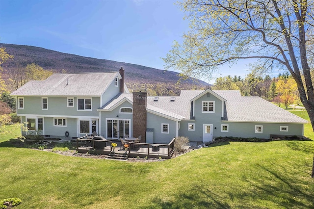 back of property with a deck with mountain view, a yard, and a chimney