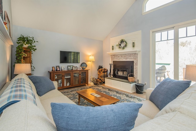 living area with a fireplace with raised hearth, high vaulted ceiling, and wood finished floors