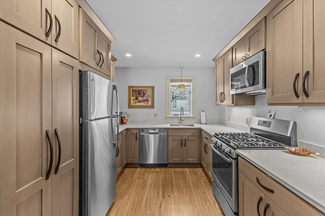 kitchen with appliances with stainless steel finishes, a sink, light countertops, light wood-style flooring, and recessed lighting