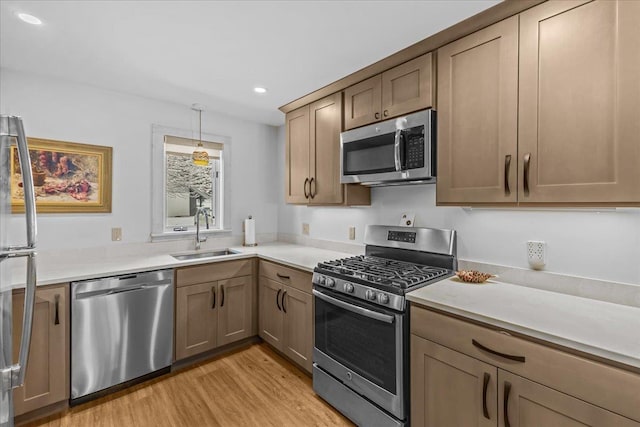 kitchen featuring recessed lighting, light countertops, a sink, light wood-style flooring, and appliances with stainless steel finishes