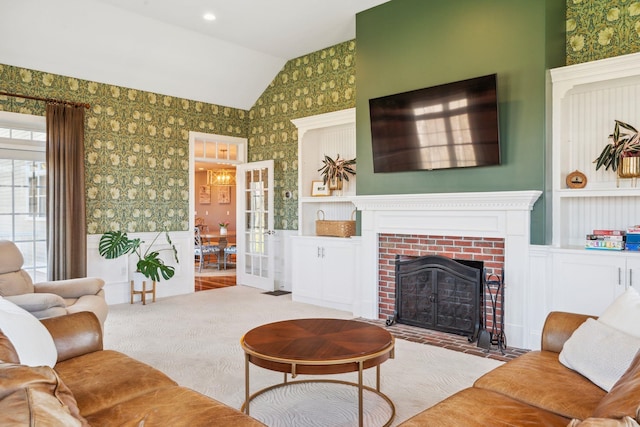 living room featuring wainscoting, a brick fireplace, lofted ceiling, wallpapered walls, and french doors