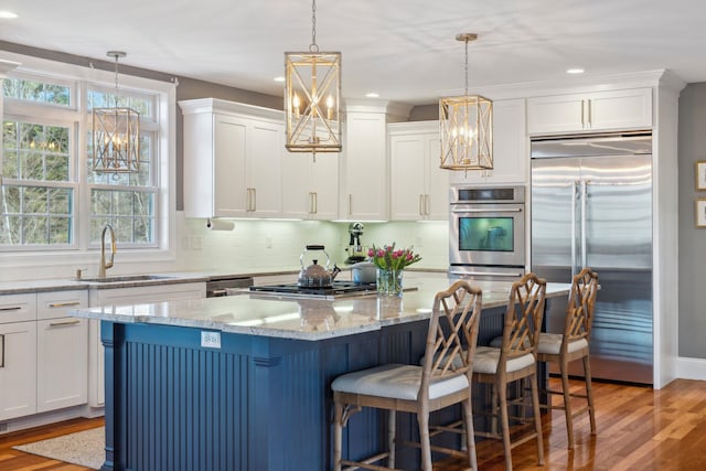 kitchen with an inviting chandelier, white cabinets, a sink, light wood finished floors, and stainless steel appliances