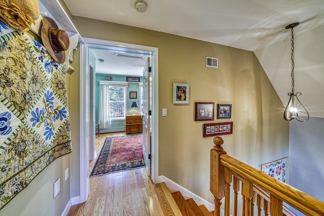 hall featuring visible vents, baseboards, and wood finished floors
