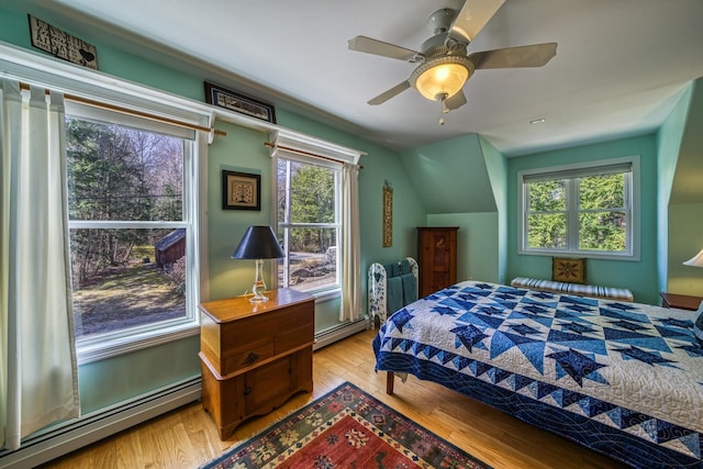 bedroom with a baseboard radiator, vaulted ceiling, light wood finished floors, and ceiling fan