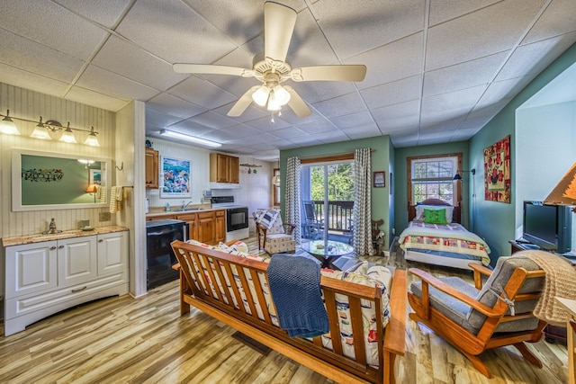 living area featuring light wood-style floors, a ceiling fan, a paneled ceiling, and wooden walls