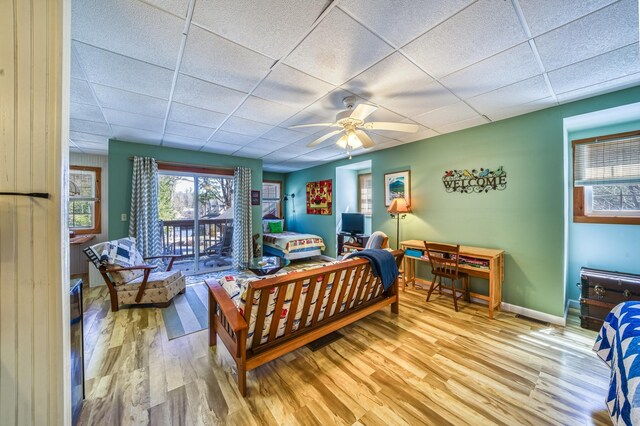 bedroom featuring ceiling fan, access to exterior, baseboards, a drop ceiling, and wood finished floors