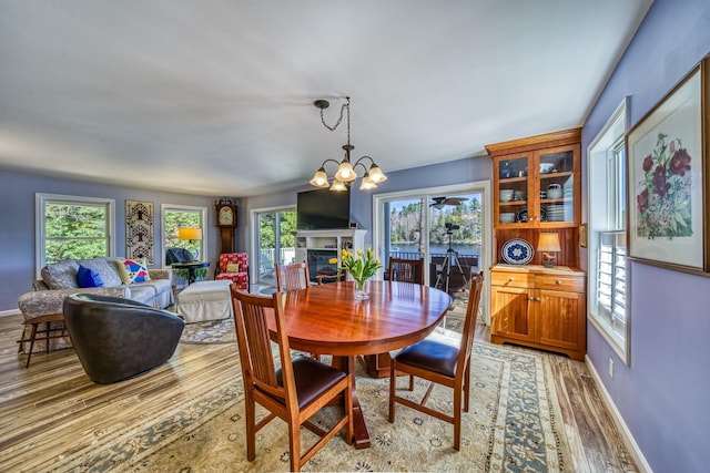 dining room featuring baseboards, an inviting chandelier, light wood finished floors, and a fireplace