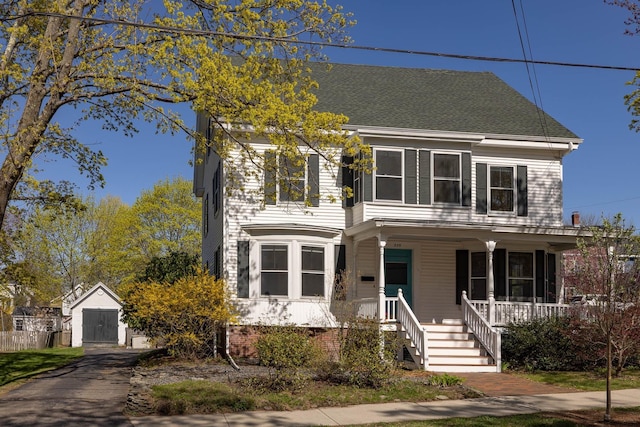colonial home featuring covered porch, a shingled roof, and an outbuilding