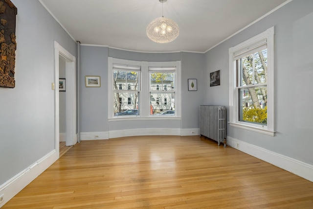 empty room with crown molding, an inviting chandelier, radiator, baseboards, and light wood-style flooring
