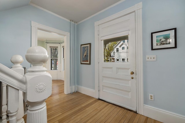 doorway with light wood-style floors, ornamental molding, and baseboards