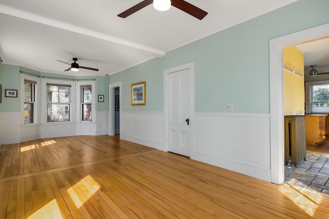 unfurnished living room with a wainscoted wall, a ceiling fan, and light wood-style flooring