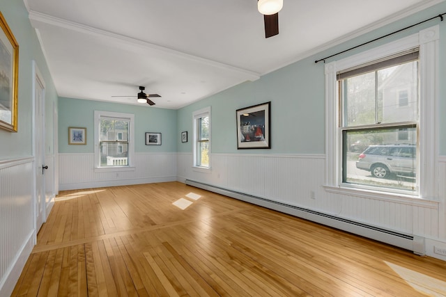 spare room featuring a wainscoted wall, ceiling fan, baseboard heating, and light wood-style flooring